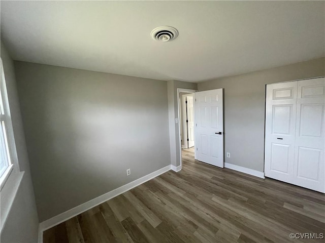 unfurnished bedroom with a closet, visible vents, baseboards, and dark wood-style flooring