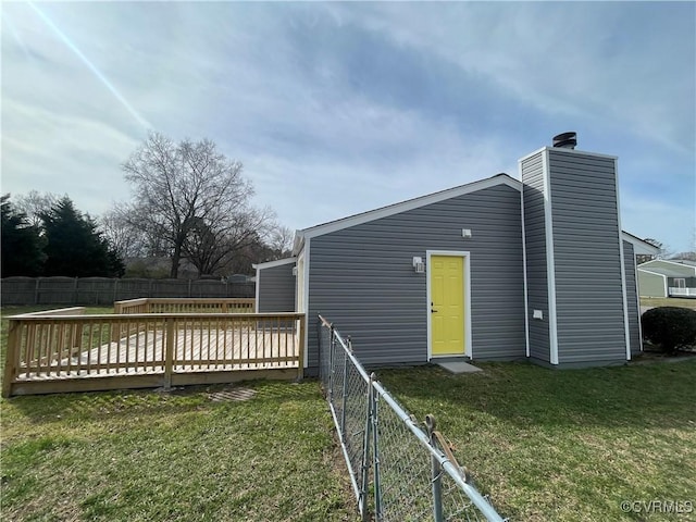 back of property with a fenced backyard, a wooden deck, a chimney, and a yard