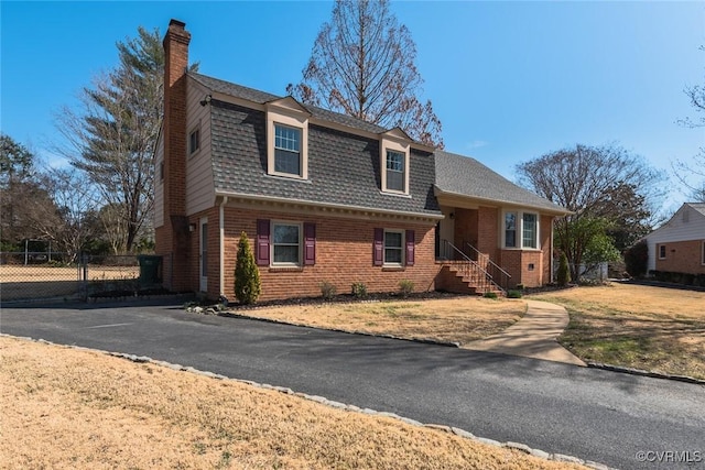 view of front of house featuring brick siding, a chimney, roof with shingles, and fence