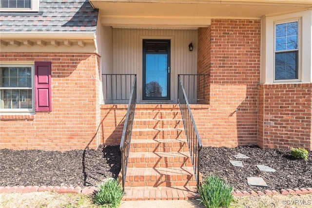 view of exterior entry with brick siding and roof with shingles