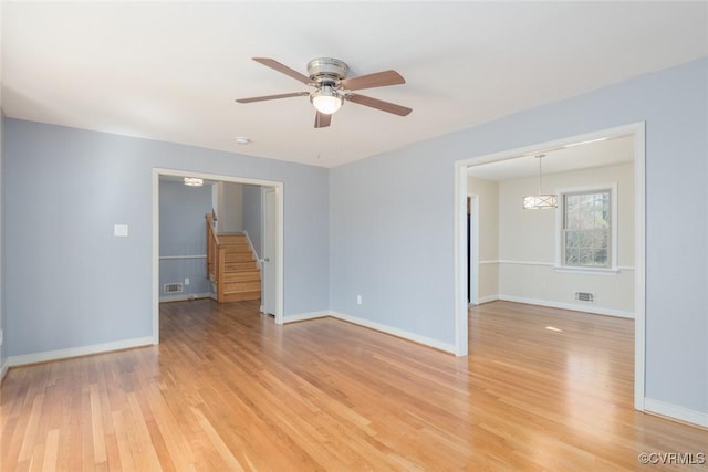 empty room with light wood finished floors, visible vents, baseboards, stairway, and a ceiling fan