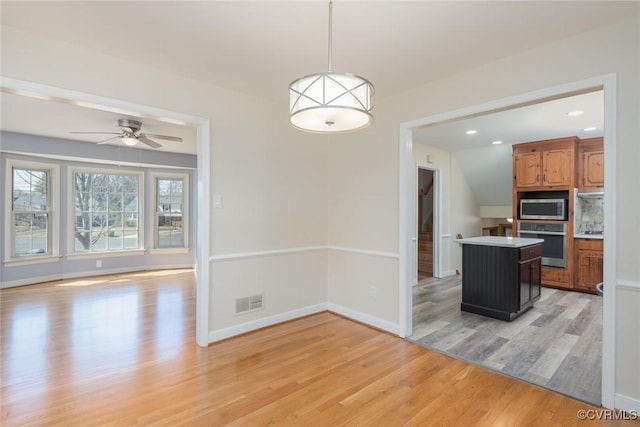 kitchen with light wood-type flooring, stainless steel appliances, brown cabinetry, decorative backsplash, and baseboards