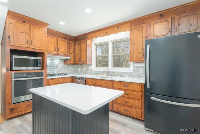 kitchen featuring under cabinet range hood, tasteful backsplash, appliances with stainless steel finishes, light wood finished floors, and light countertops