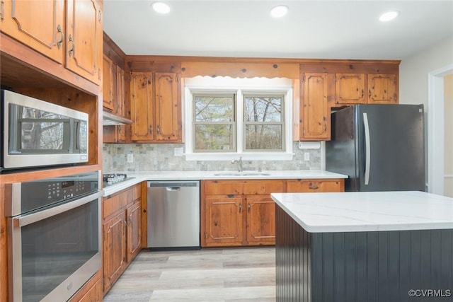 kitchen with decorative backsplash, recessed lighting, appliances with stainless steel finishes, brown cabinetry, and a sink