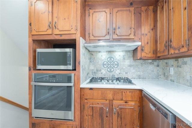 kitchen with light countertops, backsplash, under cabinet range hood, and stainless steel appliances