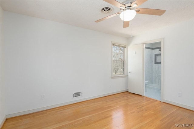 unfurnished bedroom with ensuite bath, wood finished floors, visible vents, and baseboards