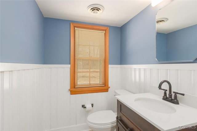 bathroom with a wainscoted wall, toilet, and visible vents