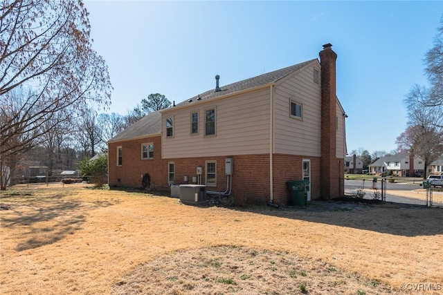 rear view of house with brick siding, fence, central air condition unit, a chimney, and a gate