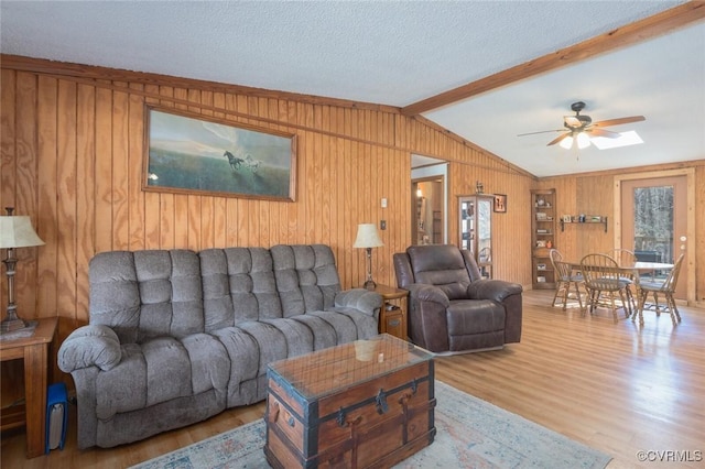 living area with lofted ceiling with beams, a textured ceiling, wood finished floors, wood walls, and ceiling fan