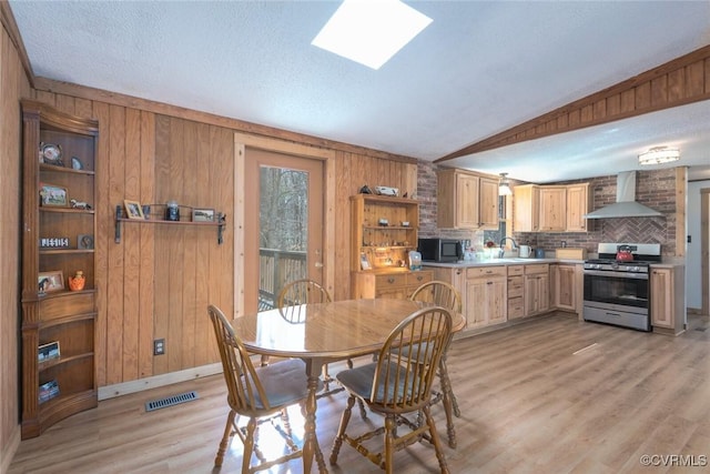 dining space with visible vents, lofted ceiling with skylight, wooden walls, and light wood-style flooring