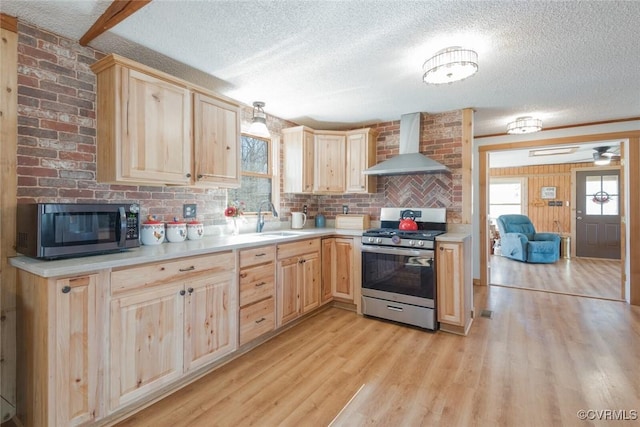 kitchen featuring a sink, light brown cabinetry, stainless steel appliances, wall chimney range hood, and a wealth of natural light