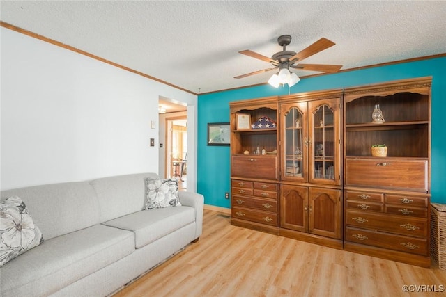 living area featuring ceiling fan, light wood-style flooring, ornamental molding, and a textured ceiling