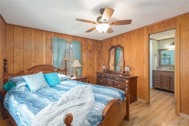 bedroom featuring wooden walls, a ceiling fan, light wood finished floors, and a textured ceiling