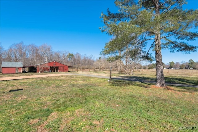 view of yard featuring an outdoor structure, a detached garage, a rural view, and driveway