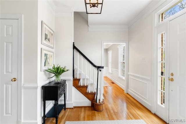 foyer entrance with crown molding, stairway, wainscoting, wood finished floors, and a decorative wall