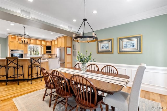 dining room with a chandelier, a wainscoted wall, light wood-style flooring, and crown molding