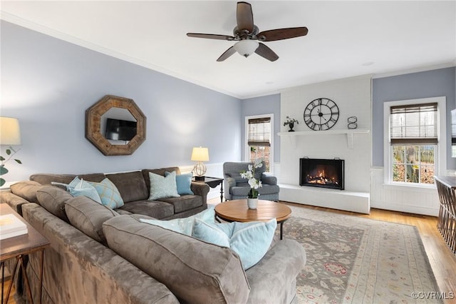 living room with a wealth of natural light, crown molding, light wood-type flooring, and a lit fireplace