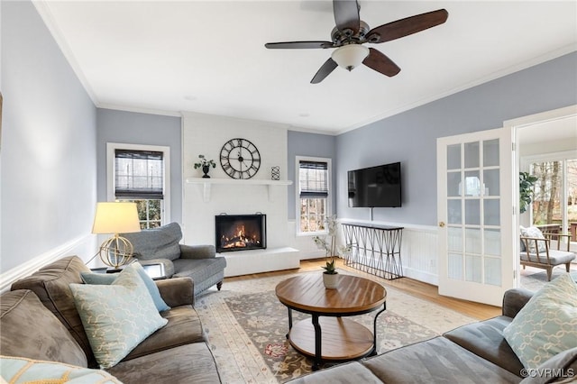 living room featuring baseboards, ceiling fan, ornamental molding, a warm lit fireplace, and wood finished floors