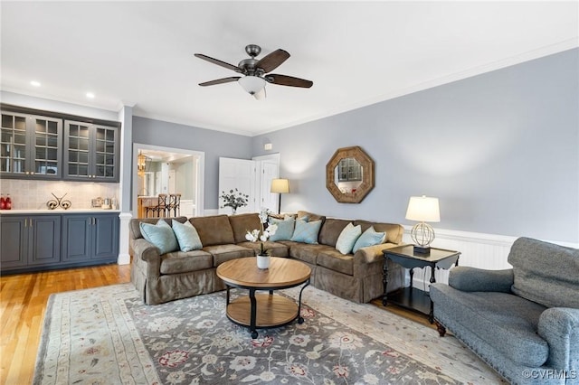 living room with a ceiling fan, recessed lighting, ornamental molding, wainscoting, and light wood-type flooring