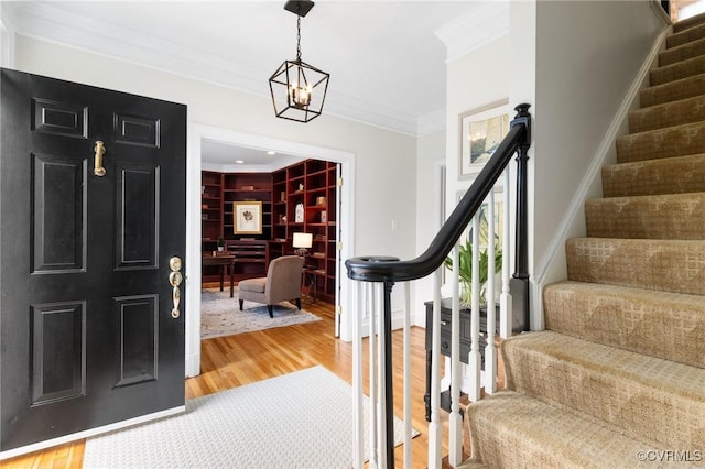 entrance foyer with stairs, an inviting chandelier, wood finished floors, and crown molding