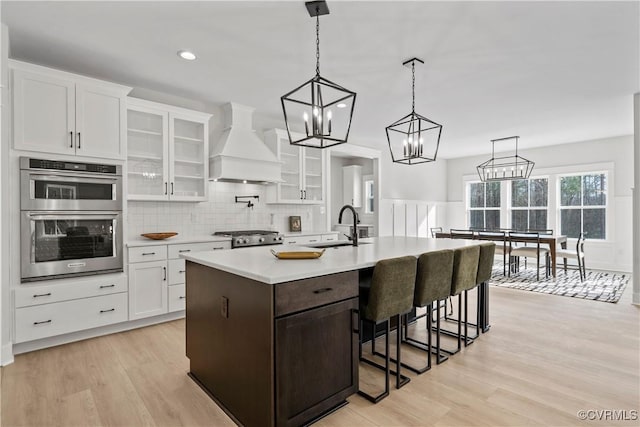 kitchen featuring a sink, light countertops, custom range hood, white cabinetry, and double oven