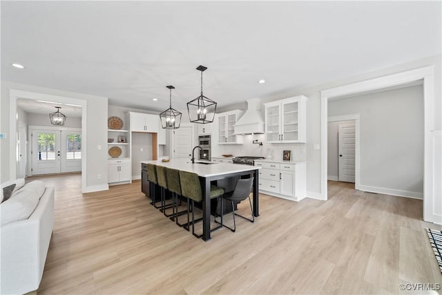 kitchen featuring custom exhaust hood, light countertops, white cabinetry, light wood-type flooring, and a kitchen bar