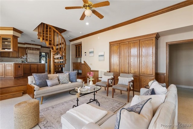 living room with stairs, a ceiling fan, ornamental molding, and wainscoting