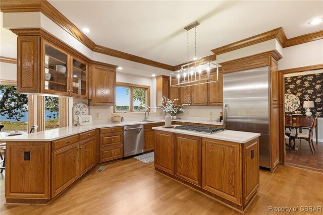 kitchen featuring light wood-type flooring, brown cabinets, appliances with stainless steel finishes, a peninsula, and light countertops