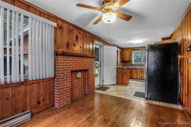 kitchen with freestanding refrigerator, light wood-style floors, wooden walls, brown cabinetry, and a baseboard radiator