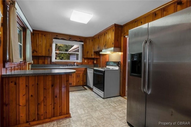 kitchen with dark countertops, stainless steel fridge with ice dispenser, under cabinet range hood, dishwasher, and range with gas stovetop