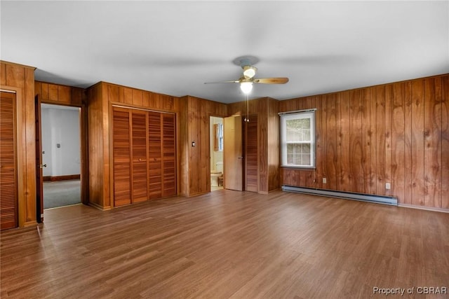 interior space with wooden walls, wood finished floors, a ceiling fan, and a baseboard radiator