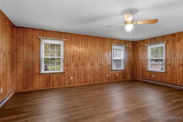 empty room with a baseboard heating unit, a healthy amount of sunlight, and wood finished floors