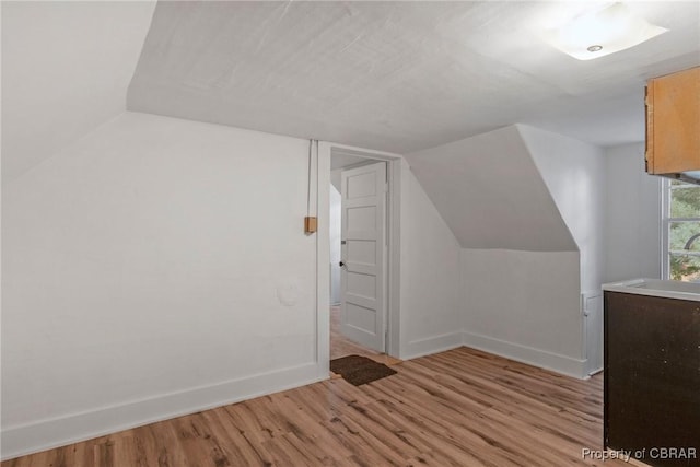 bonus room featuring a sink, baseboards, lofted ceiling, and light wood-style flooring