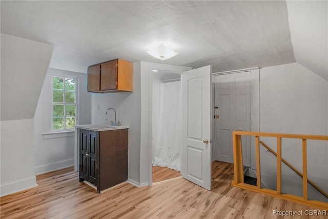 additional living space featuring a sink, baseboards, vaulted ceiling, and light wood finished floors