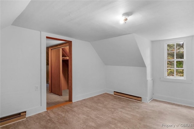 additional living space featuring visible vents, a baseboard heating unit, baseboards, vaulted ceiling, and wood finished floors