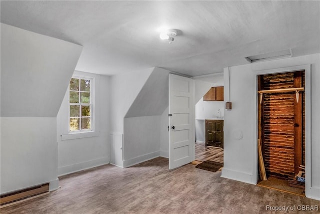 additional living space with wood finished floors, baseboards, attic access, vaulted ceiling, and a baseboard heating unit