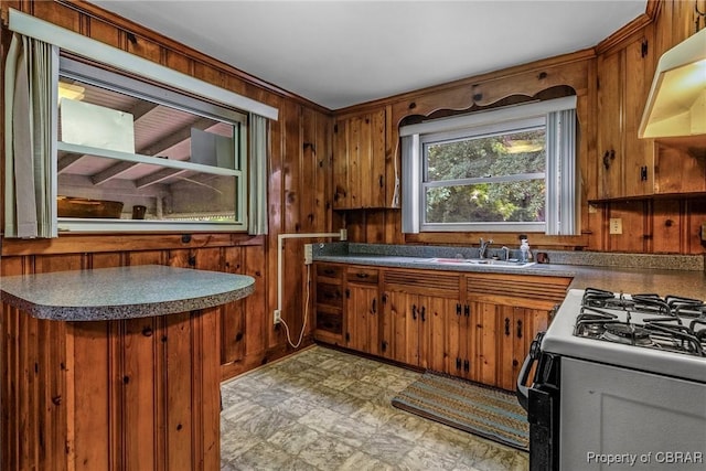 kitchen featuring range with gas stovetop, wooden walls, brown cabinetry, under cabinet range hood, and dark countertops