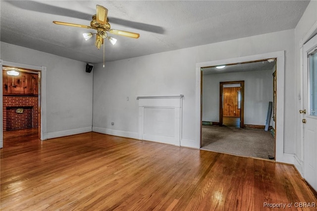 unfurnished living room with ceiling fan, baseboards, a textured ceiling, and wood finished floors