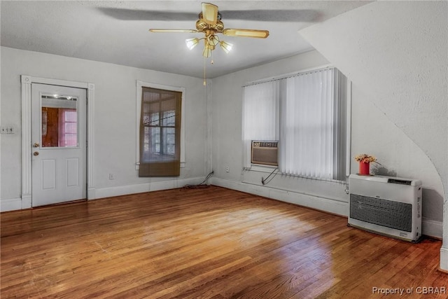 unfurnished bedroom with heating unit, cooling unit, a ceiling fan, baseboards, and wood-type flooring