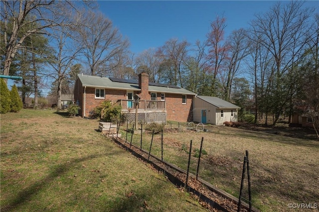 back of property with a wooden deck, solar panels, a chimney, a lawn, and brick siding