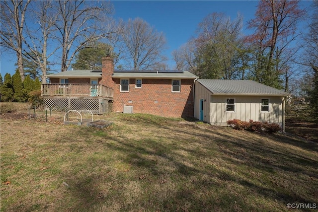 back of house with a lawn, solar panels, a deck, and a chimney