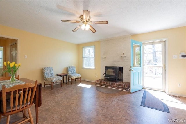 sitting room with baseboards, plenty of natural light, ceiling fan, and a wood stove