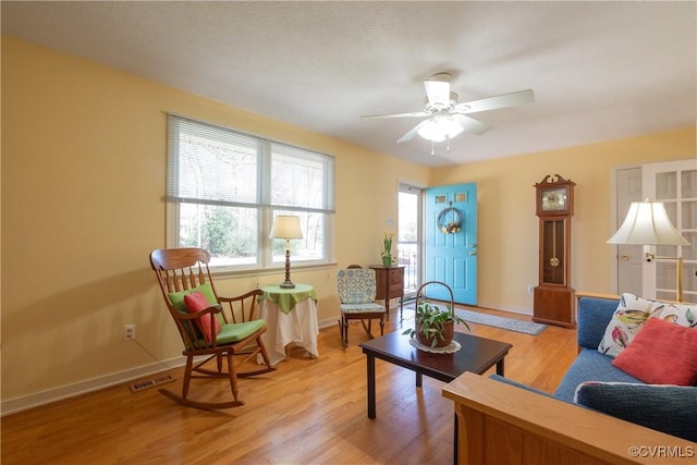 living room with light wood-type flooring, visible vents, baseboards, and ceiling fan