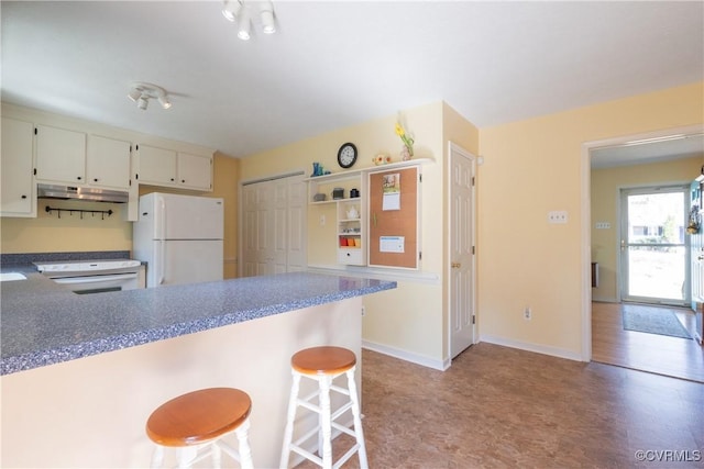 kitchen featuring under cabinet range hood, a kitchen breakfast bar, white appliances, a peninsula, and baseboards