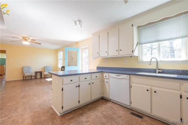 kitchen with visible vents, a peninsula, white dishwasher, a sink, and dark countertops