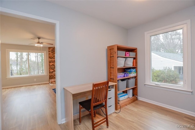 office space featuring light wood finished floors, a healthy amount of sunlight, baseboards, and ceiling fan