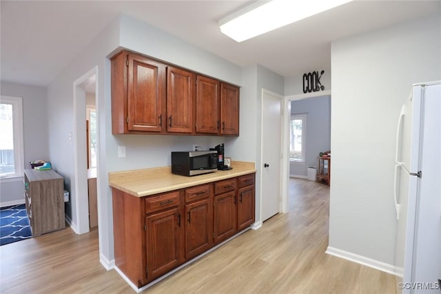 kitchen featuring brown cabinetry, light wood finished floors, freestanding refrigerator, light countertops, and stainless steel microwave