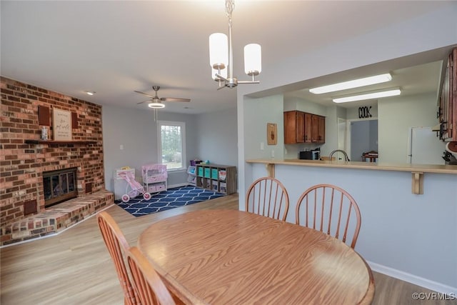 dining room featuring baseboards, ceiling fan with notable chandelier, a fireplace, and light wood finished floors