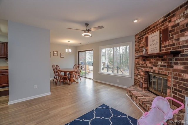 living room featuring a brick fireplace, baseboards, a ceiling fan, and wood finished floors