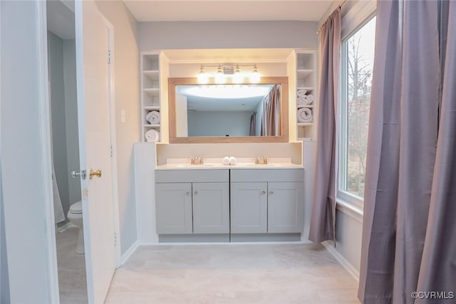 full bathroom with double vanity, toilet, baseboards, and a sink